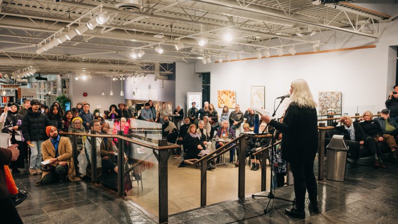 A person stands at the top of a set of stairs and speaks into a microphone to a crowd of people.