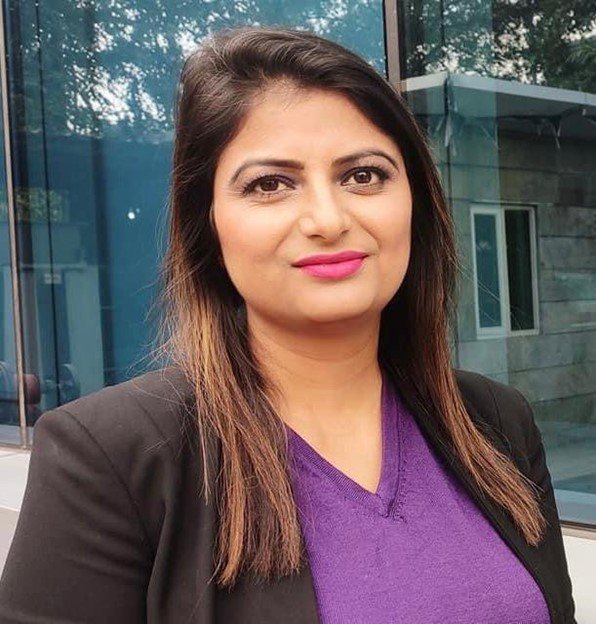 geetanjali-p-volunteer.jpg Woman in a black blazer and purple top standing outside a modern building.