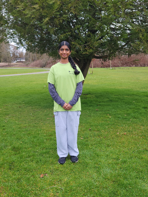 imani-s-volunteer.png Girl standing on grass in a green “Surrey Volunteer” shirt with a large tree behind her.