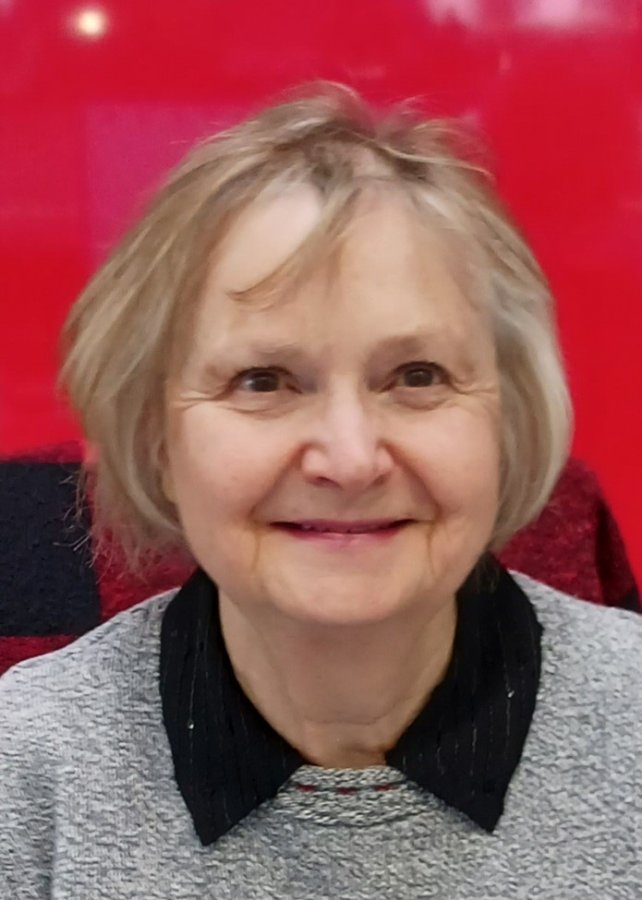 kathleen-p-volunteer.jpg Older woman smiling in front of a red wall.