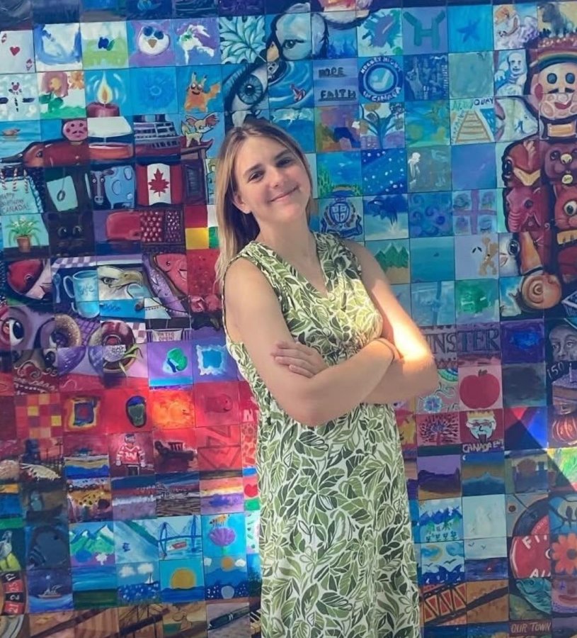 kayla-l-volunteer.jpg Woman in a leafy dress standing in front of a colourful mural.
